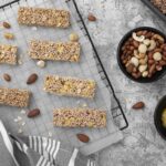 Barres de céréales anti-cholestérol maison à base d’avoine, noix et graines, posées sur une grille avec miel et fruits à coque.