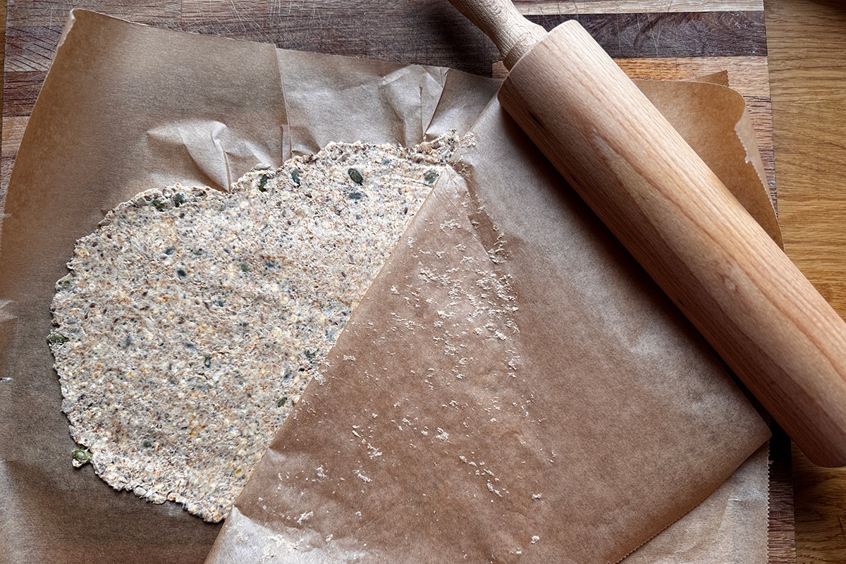 Pâte à crackers maison étalée finement entre deux feuilles de papier cuisson
