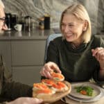 Couple partageant un repas convivial avec des tartines de saumon, illustrant qu’on peut manger normalement quand on a du cholestérol